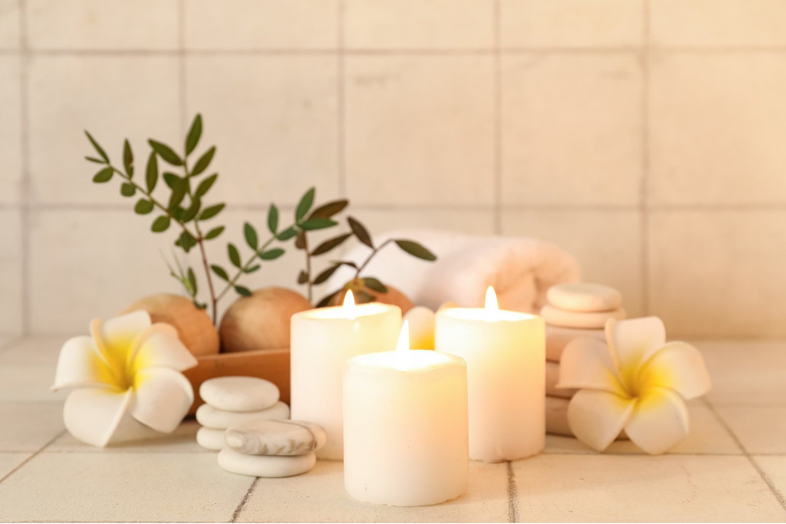 Glowing spa candles, white frangipani flowers, smooth stones, and fresh greenery