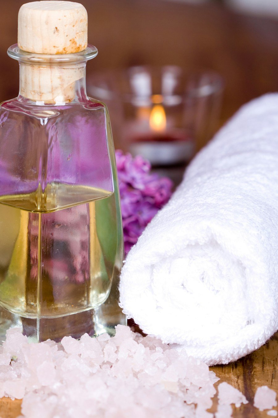 A glass bottle of massage oil next to a soft white towel
